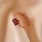 Adjustable rose gold ring with a heart-shaped garnet centerpiece, displayed on a clean white background.