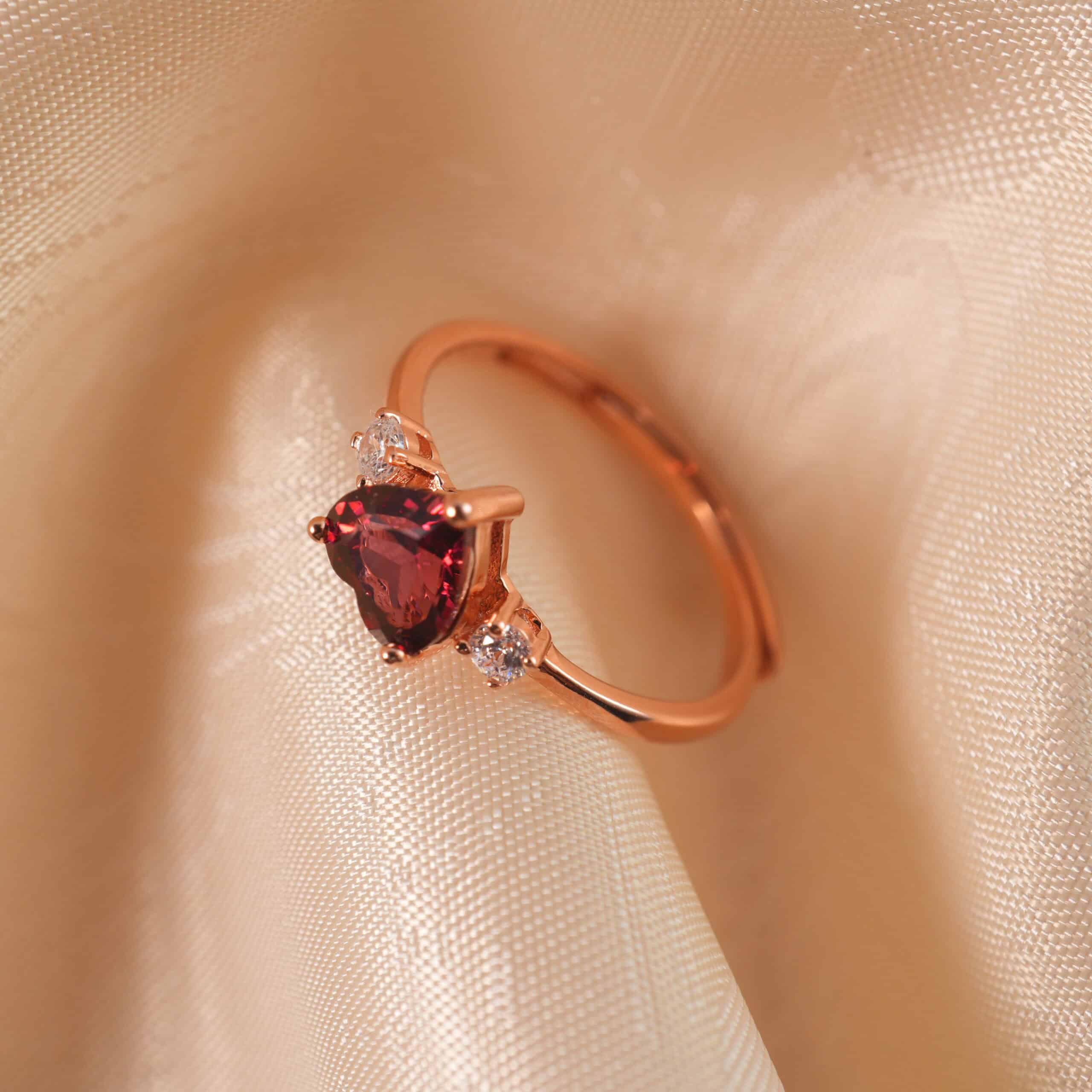 adjustable-rose-gold-garnet-heart-ring-main Adjustable rose gold ring with a heart-shaped garnet centerpiece, displayed on a clean white background.