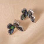 A pair of butterfly-shaped moonstone stud earrings on a white background, displaying a soft iridescent glow.