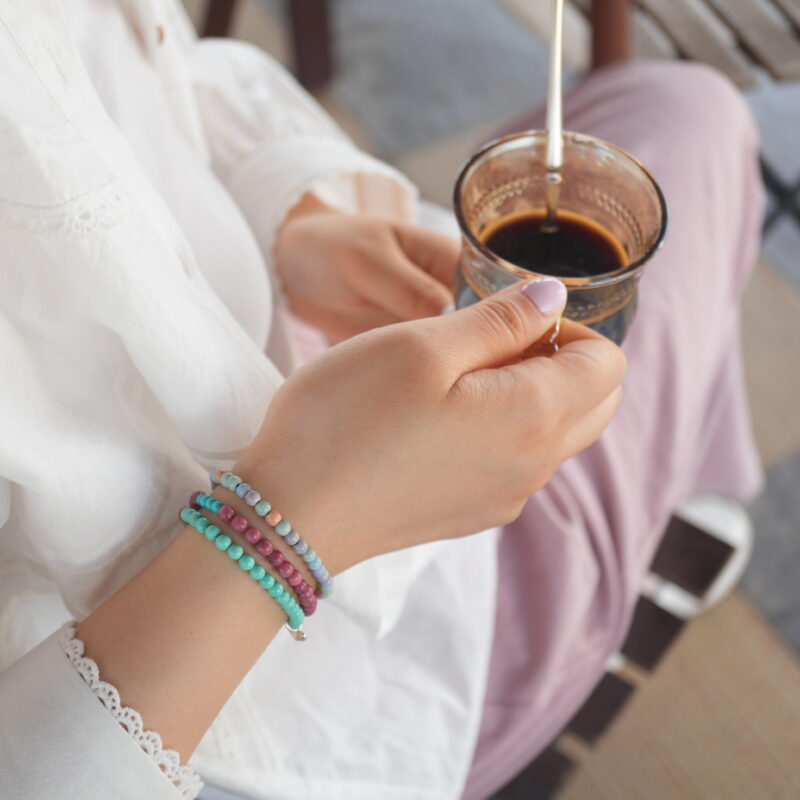 Woman holding a coffee cup wearing three stacked crystal beaded bracelets by My Starry Sky