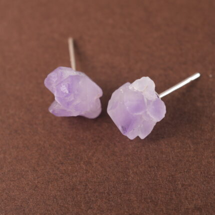 A pair of raw amethyst stud earrings displayed on a plain background, highlighting their natural and rustic texture.