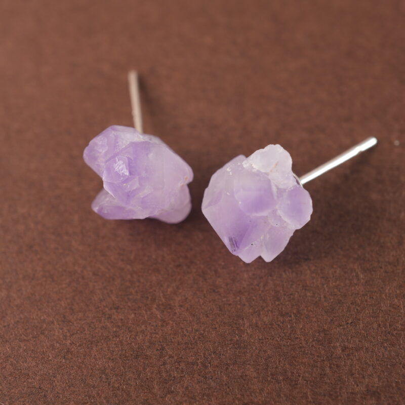 A pair of raw amethyst stud earrings displayed on a plain background, highlighting their natural and rustic texture.