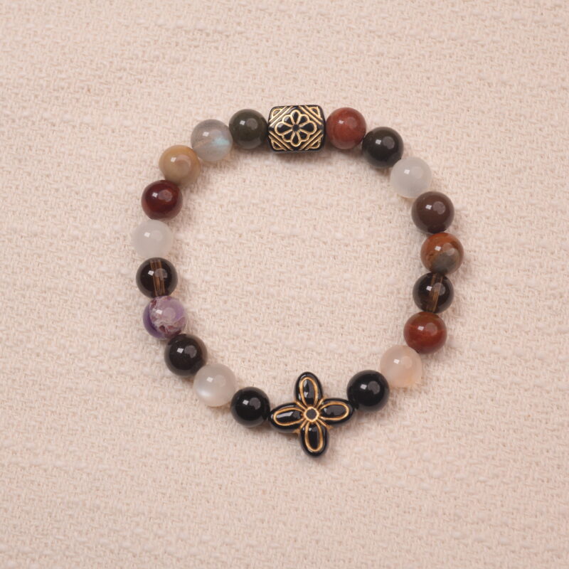 Multicolor gemstone bracelet with a black and gold patterned bead, photographed under soft daylight on a neutral background.