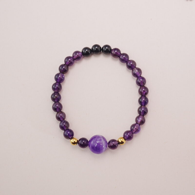 Amethyst and black tourmaline bracelet with gold accent beads, photographed under soft daylight on a neutral background.