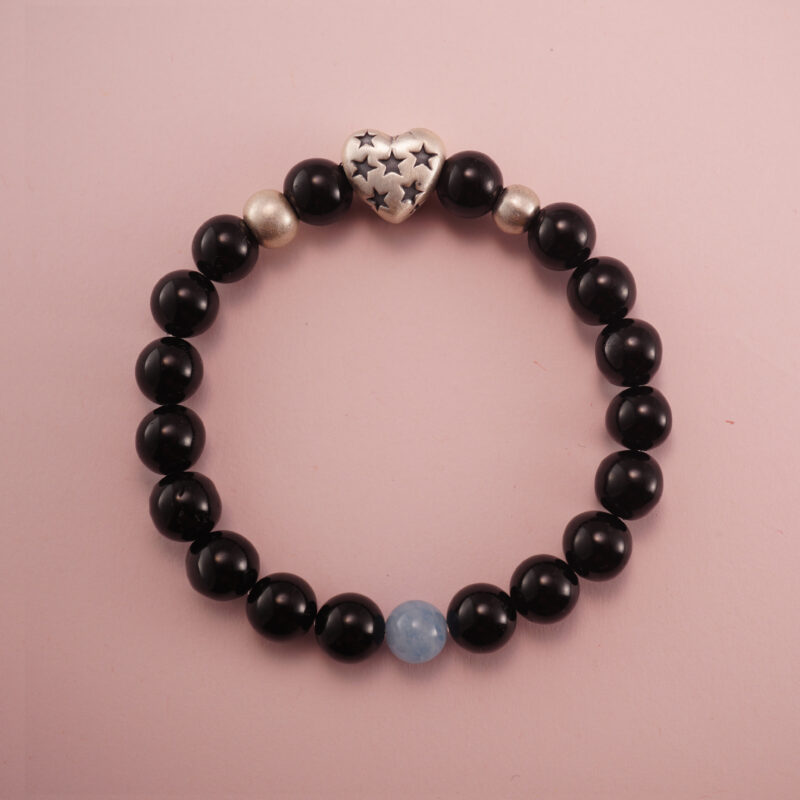 Black obsidian and aquamarine bracelet with a silver heart accent bead, photographed under soft daylight on a pink background.