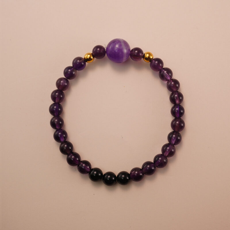 Amethyst and black tourmaline bracelet with gold accent beads, photographed under soft daylight on a neutral background.