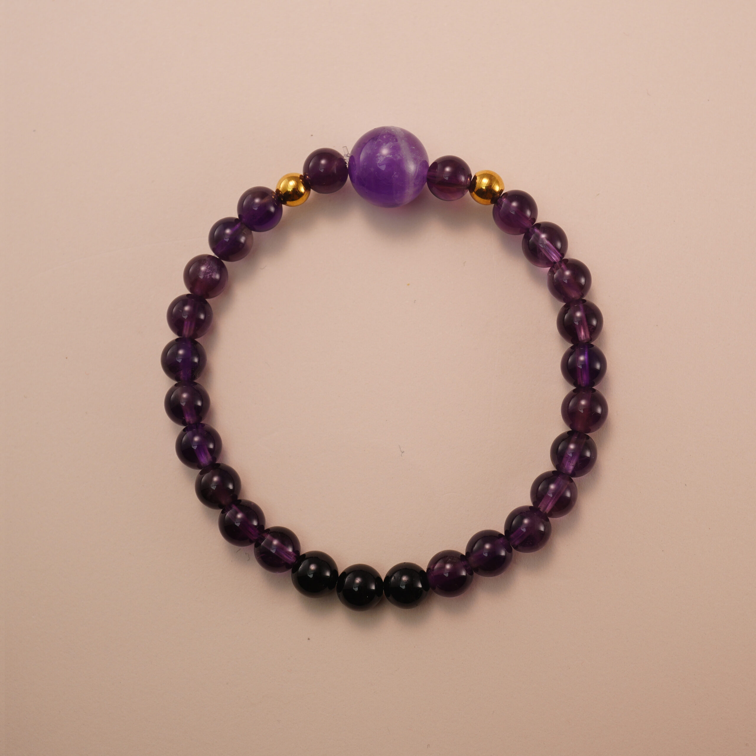 amethyst-black-tourmaline-bracelet-with-gold-beads Amethyst and black tourmaline bracelet with gold accent beads, photographed under soft daylight on a neutral background.