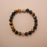 Tiger’s eye and white chalcedony bracelet with a silver fish accent bead, photographed under soft daylight to highlight the natural golden and creamy tones of the gemstones.