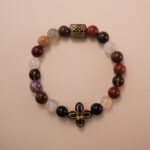 Multicolor gemstone bracelet with a black and gold patterned bead, photographed under soft daylight on a neutral background.