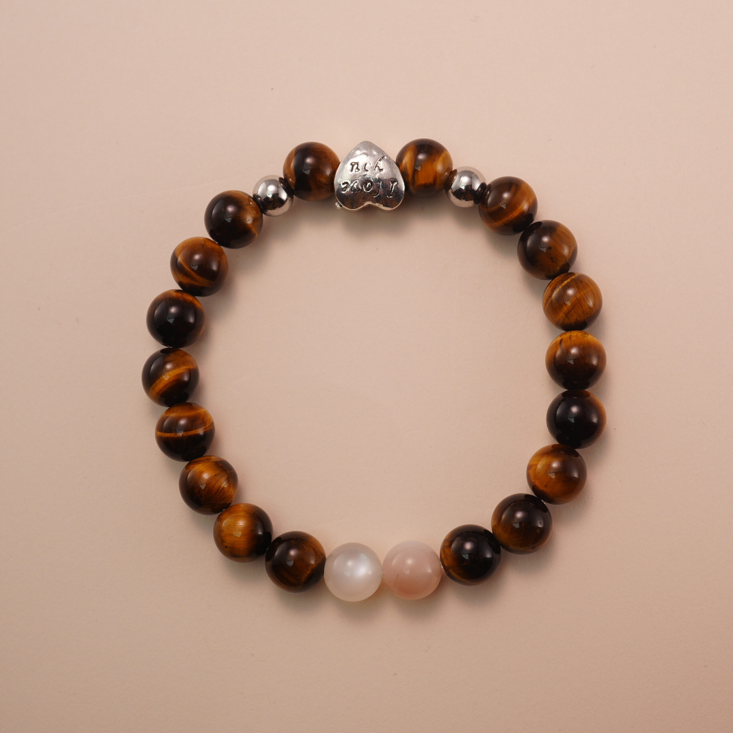 tigers-eye-moonstone-bracelet-with-silver-heart-bead Tiger’s eye and moonstone bracelet with a silver heart accent bead, photographed under soft daylight to highlight the warm golden and soft white tones.