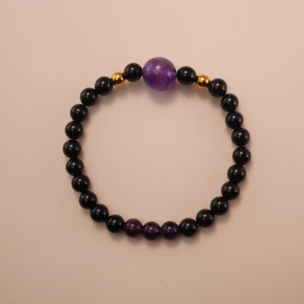 Amethyst and black tourmaline bracelet with gold accent beads, photographed under soft daylight on a neutral background.
