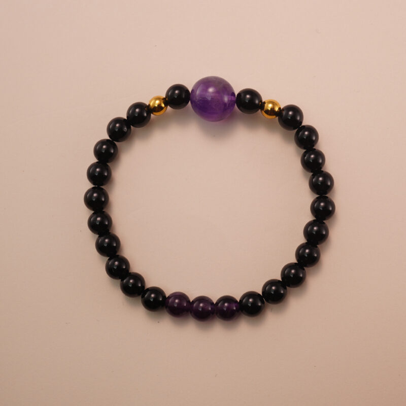 Amethyst and black tourmaline bracelet with gold accent beads, photographed under soft daylight on a neutral background.