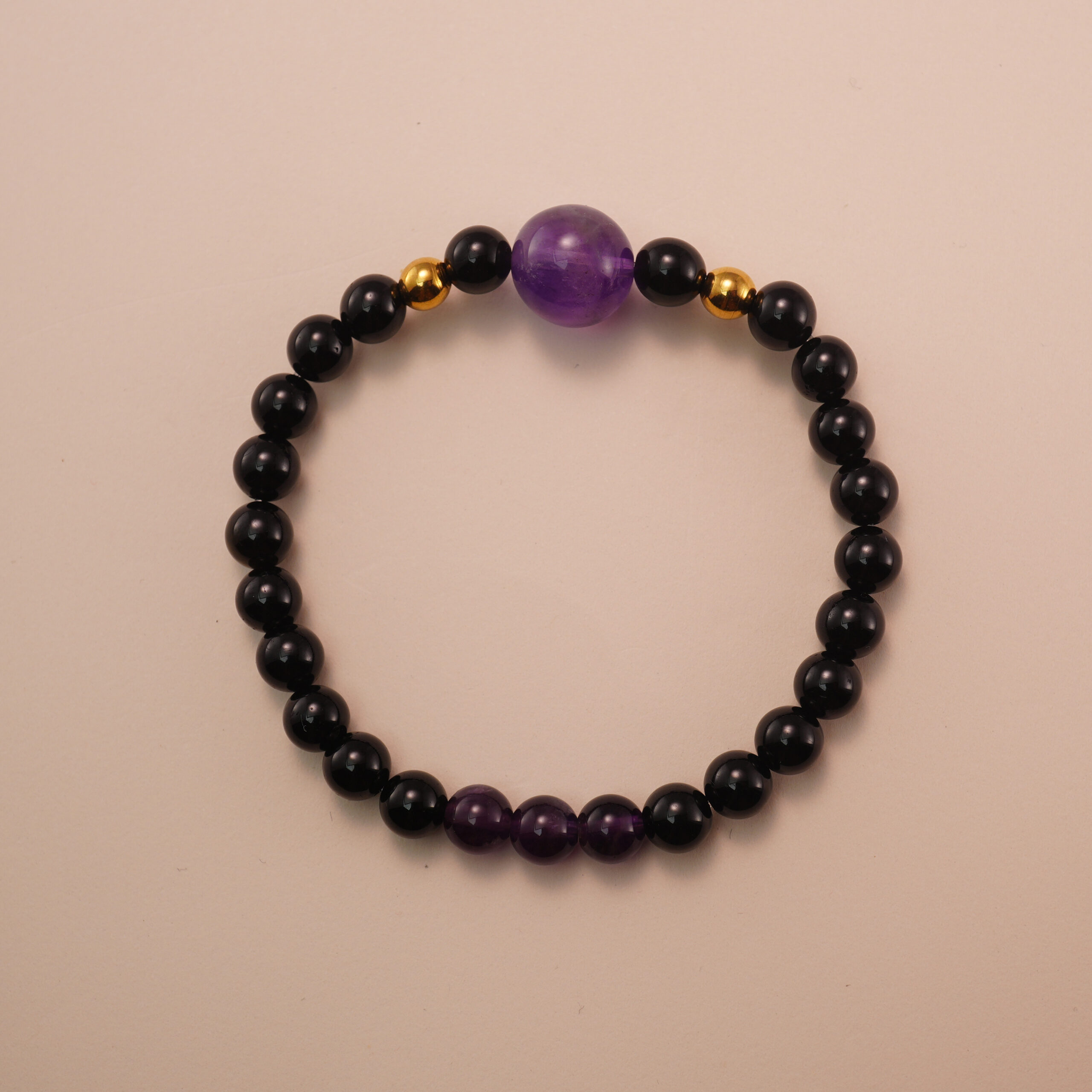 black-tourmaline-and-amethyst-bracelet-with-gold-beads Amethyst and black tourmaline bracelet with gold accent beads, photographed under soft daylight on a neutral background.