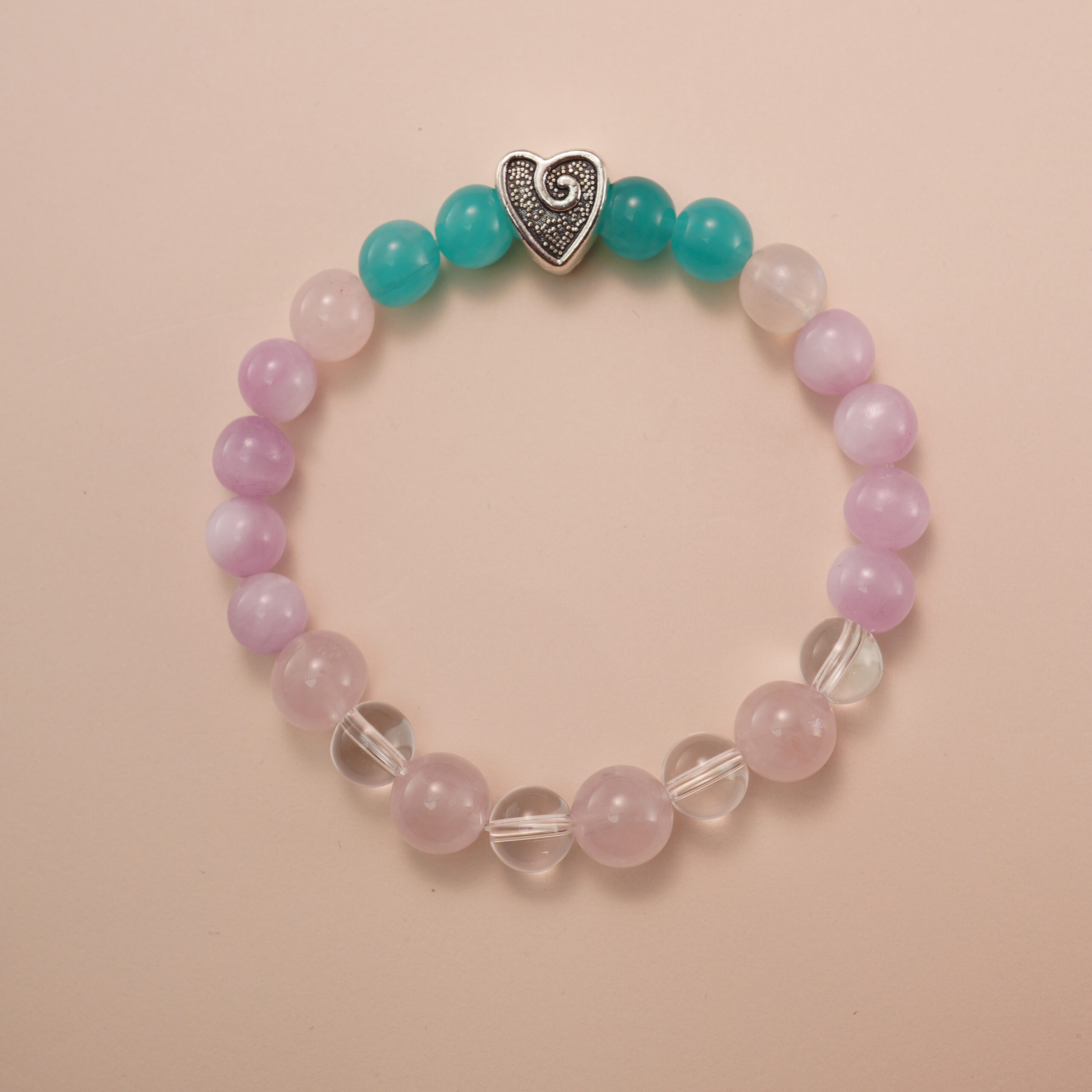 kunzite-and- amazonite-and-clear-quartz-bracelet-with-heart-clasp Kunzite, amazonite, and clear quartz bracelet with a silver heart accent bead, photographed under soft daylight to highlight the pastel purple, aqua green, and translucent white tones.