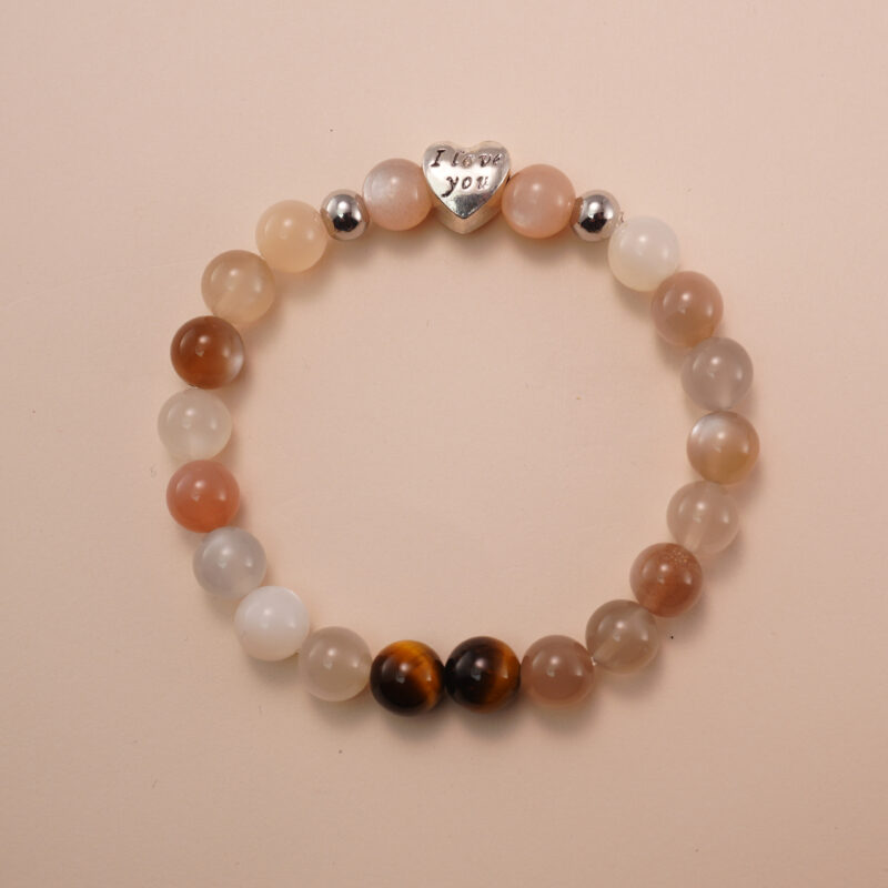 Rainbow moonstone and tiger’s eye bracelet with a silver heart bead engraved with “I love you,” photographed under soft daylight to highlight the iridescent white and golden-brown hues.
