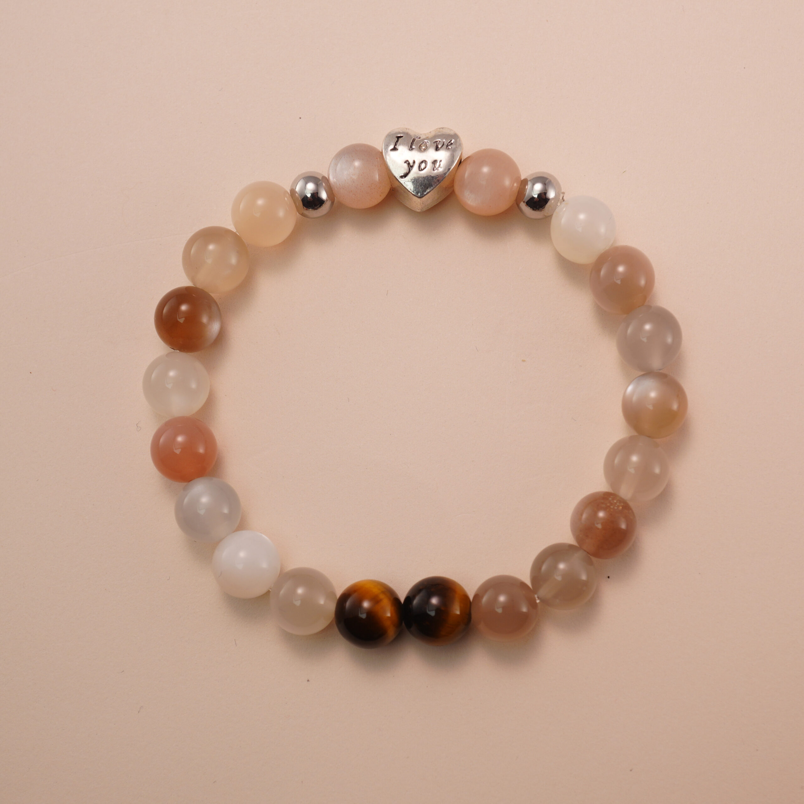 rainbow-moonstone-tigers-eye-bracelet-with-silver-heart Rainbow moonstone and tiger’s eye bracelet with a silver heart bead engraved with “I love you,” photographed under soft daylight to highlight the iridescent white and golden-brown hues.