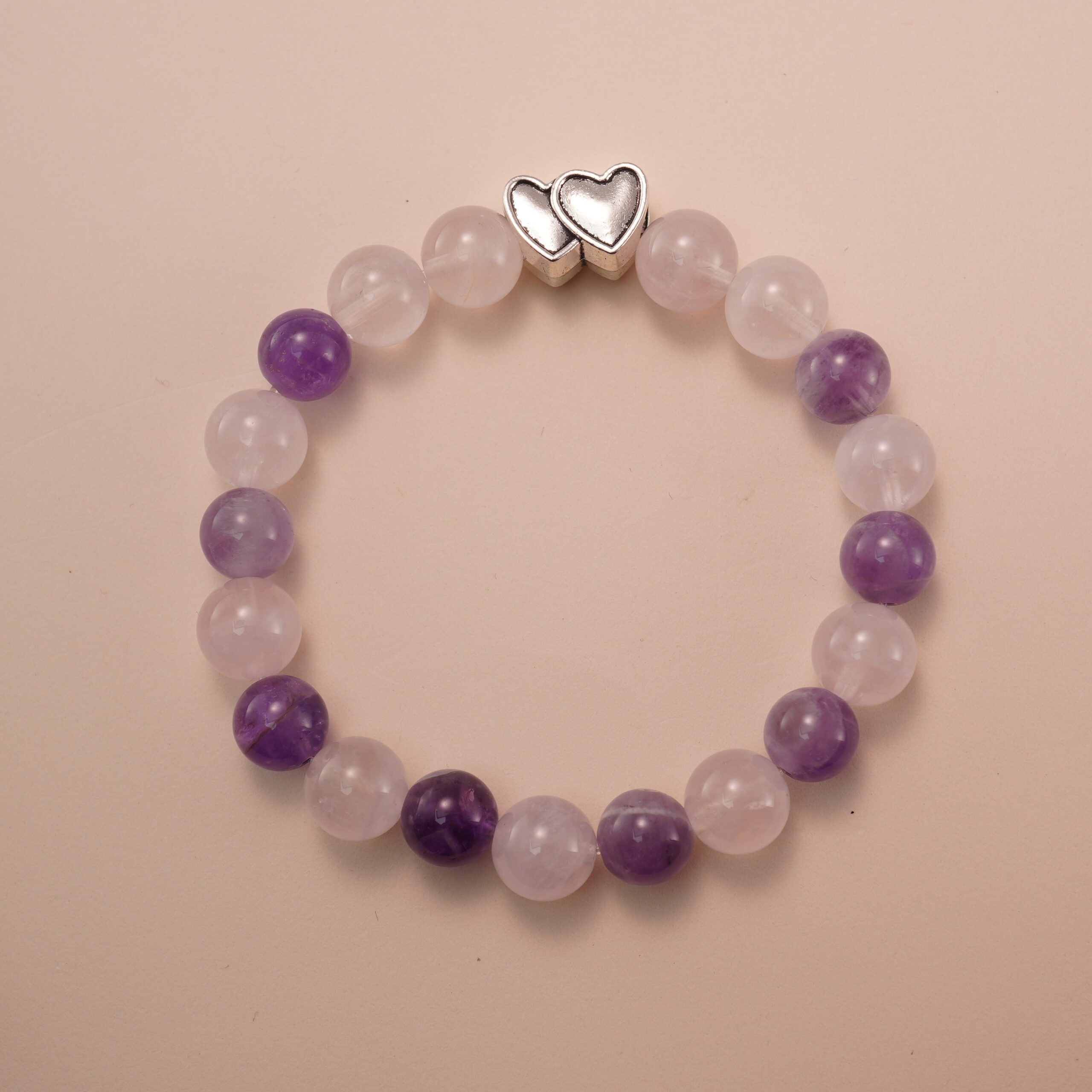 amethyst-rose-quartz-bracelet-with-silver-double-heart Amethyst and rose quartz bracelet with a silver double-heart bead, photographed under soft daylight to highlight the gentle pink and purple hues of the gemstones.