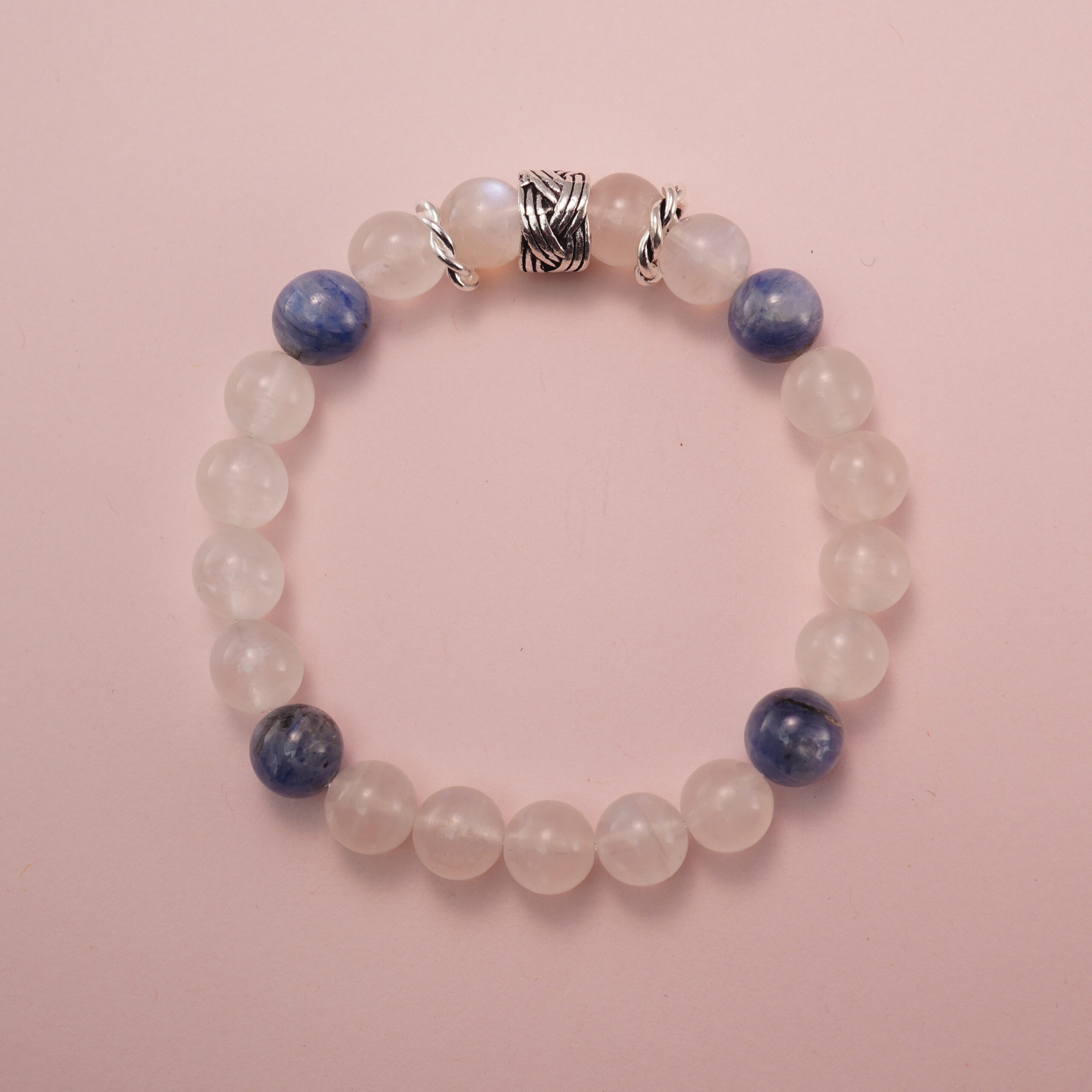 moonstone-kyanite-bracelet-natural-light Moonstone and kyanite bracelet photographed under soft daylight on a pink background, highlighting the milky white glow of moonstone and the deep blue tones of kyanite.