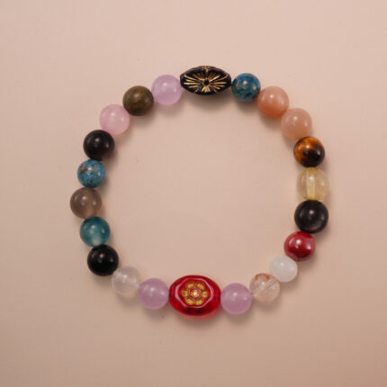 Multicolor gemstone bracelet featuring a mix of natural stones in red, blue, yellow, pink, and brown tones, photographed under soft daylight on a neutral background.