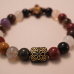 Close-up detail of multicolor gemstone bracelet featuring a black bead with intricate gold flower patterns and polished natural stones.1