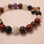 Close-up detail of multicolor gemstone bracelet featuring a black bead with intricate gold flower patterns and polished natural stones.2