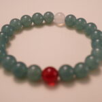 Close-up detail of green chalcedony bracelet featuring a red agate and a white chalcedony bead, showing the smooth texture and polished finish of each gemstone.