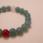 Close-up detail of green chalcedony bracelet featuring a red agate and a white chalcedony bead, showing the smooth texture and polished finish of each gemstone.