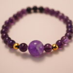 Close-up detail of amethyst and black tourmaline bracelet featuring gold accent beads, showing the smooth polish and deep natural gemstone colors.2