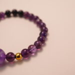 Close-up detail of amethyst and black tourmaline bracelet featuring gold accent beads, showing the smooth polish and deep natural gemstone colors.1