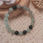 Green aventurine and black obsidian bracelet displayed in a lifestyle setting under natural light, highlighting the balance of soft green and deep black tones.