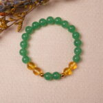 Lifestyle photo of green aventurine and citrine bracelet placed on soft fabric with warm light.