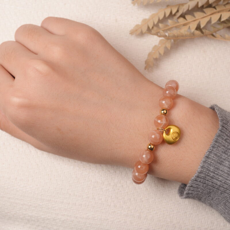 Model wearing peach moonstone bracelet with gold charm, showing an elegant and gentle look.