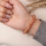 Back view of peach moonstone bracelet with gold charm, radiating soft pink glow.