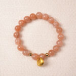 Peach moonstone bracelet with gold charm, symbolizing love, calm, and emotional balance.