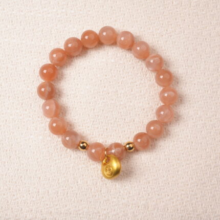 Peach moonstone bracelet with gold charm, symbolizing love, calm, and emotional balance.