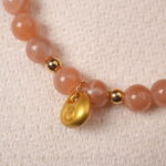 Close-up of peach moonstone bracelet with gold charm, highlighting the natural shimmer and warm tones.