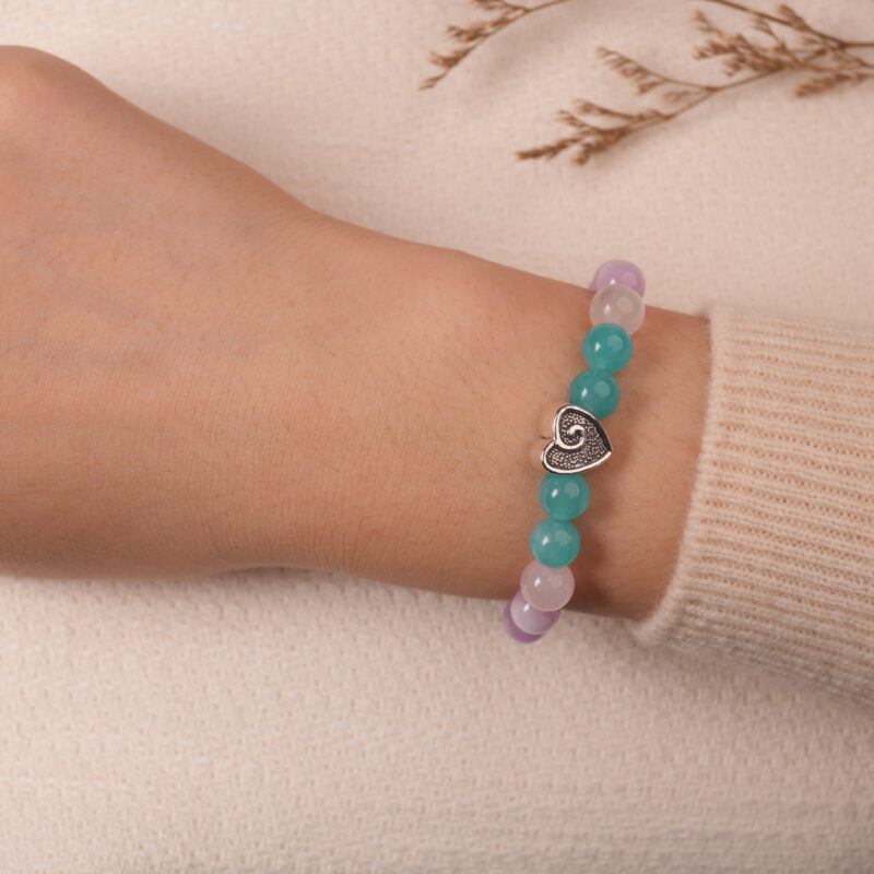 A hand wearing the Amethyst and Prehnite bracelet, showcasing the vibrant purple and green beads with a silver heart-shaped bead at the center. The bracelet is worn on a soft beige sweater, adding a stylish and calming touch.