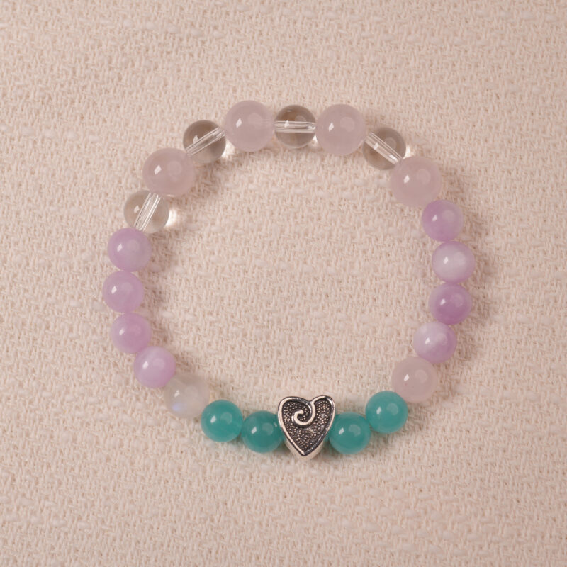 Amethyst and Prehnite bracelet featuring smooth, polished beads in shades of purple and green, with a central silver heart-shaped bead. The bracelet is displayed on a soft fabric surface, emphasizing its elegance and soothing colors.