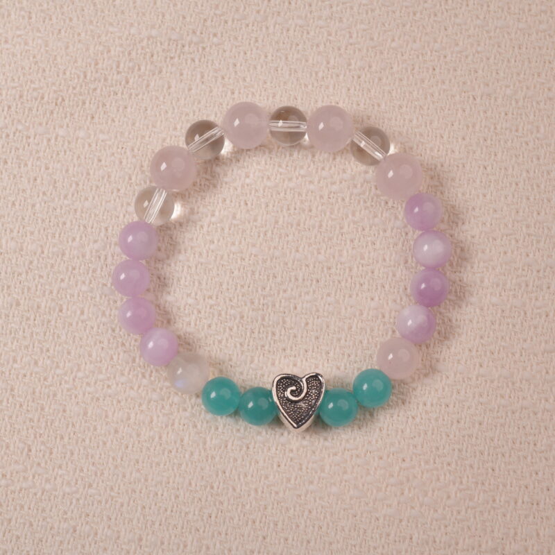 Amethyst and Prehnite bracelet featuring smooth, polished beads in shades of purple and green, with a central silver heart-shaped bead. The bracelet is displayed on a soft fabric surface, emphasizing its elegance and soothing colors.