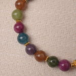 Close-up of multicolor tourmaline beads with golden details, highlighting natural brilliance and protection charm.