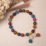 Lifestyle photo of multicolor tourmaline bracelet with gourd charm placed beside dried flowers.