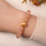 Model wearing peach moonstone bracelet with citrine and gold heart bead, exuding soft romantic charm.
