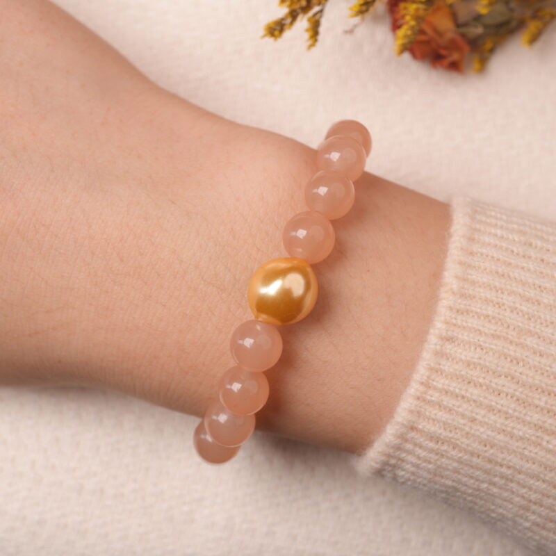 Model wearing peach moonstone bracelet with citrine and gold heart bead, exuding soft romantic charm.