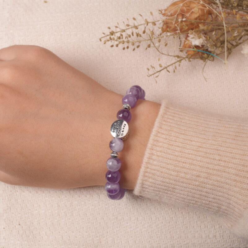 A hand wearing the Amethyst and Prehnite bracelet, featuring purple Amethyst and green Prehnite beads. The bracelet is paired with a soft beige sweater and delicate nails, adding a chic and peaceful vibe.