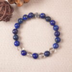 Lifestyle photo of lapis lazuli and clear quartz bracelet placed on beige fabric with natural decor.