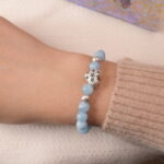 Model wearing aquamarine bracelet with silver heart charm, showing elegant blue tone and serene energy.
