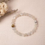 Lifestyle photo of moonstone bracelet placed beside soft beige fabric and dried flowers.