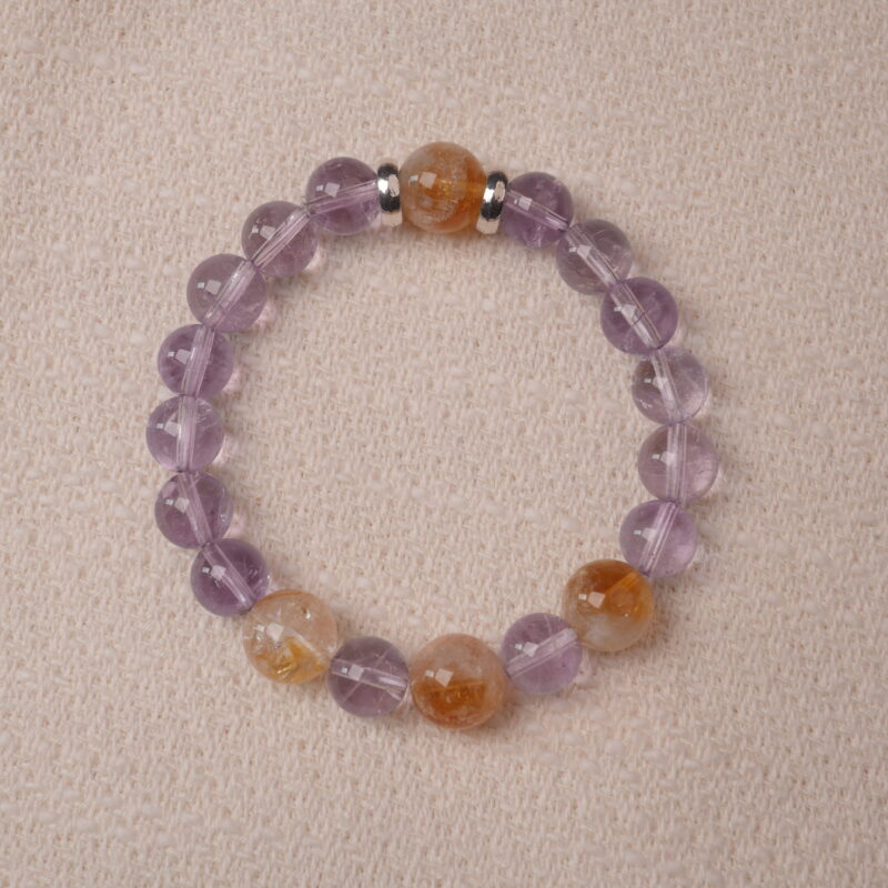 A close-up shot of an Amethyst and Citrine bracelet, featuring hexagonal-cut crystals in shades of purple and golden yellow. The bracelet is designed with silver spacers to accentuate the striking contrast between the two stones, giving it a sophisticated and vibrant look.