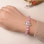Model wearing rose quartz bracelet with a delicate bow charm, exuding elegance and charm.