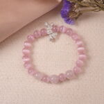 Lifestyle photo of rose quartz bow charm bracelet placed on soft fabric, symbolizing love and grace.
